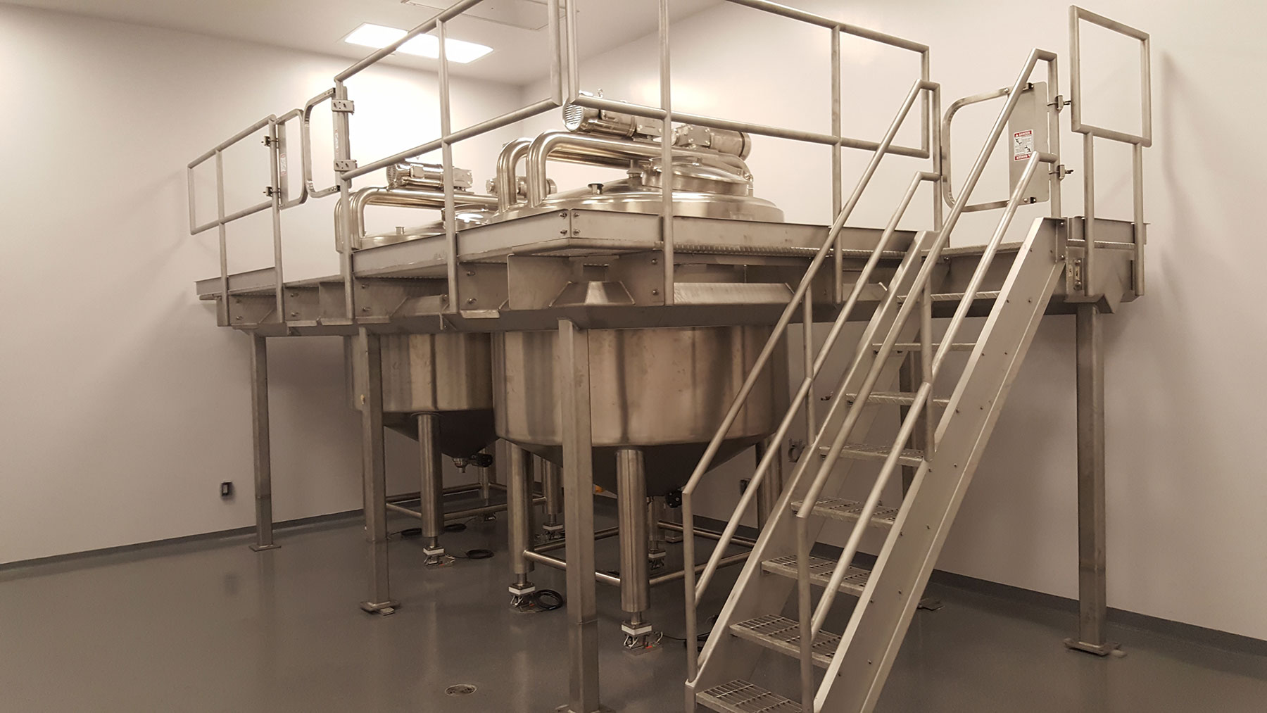 Batching tanks and platform with stainless steel construction, featuring a staircase for access, in a clean processing environment, relevant to food production automation by CHL Systems.