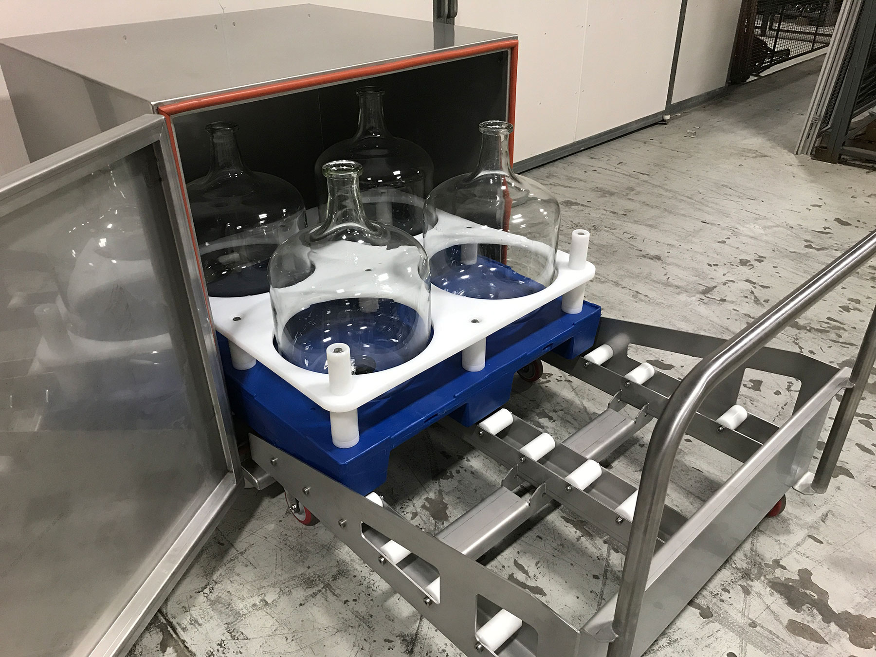 Bottle cart featuring multiple glass bottles secured on a blue base with white supports, designed for material handling in food processing automation.