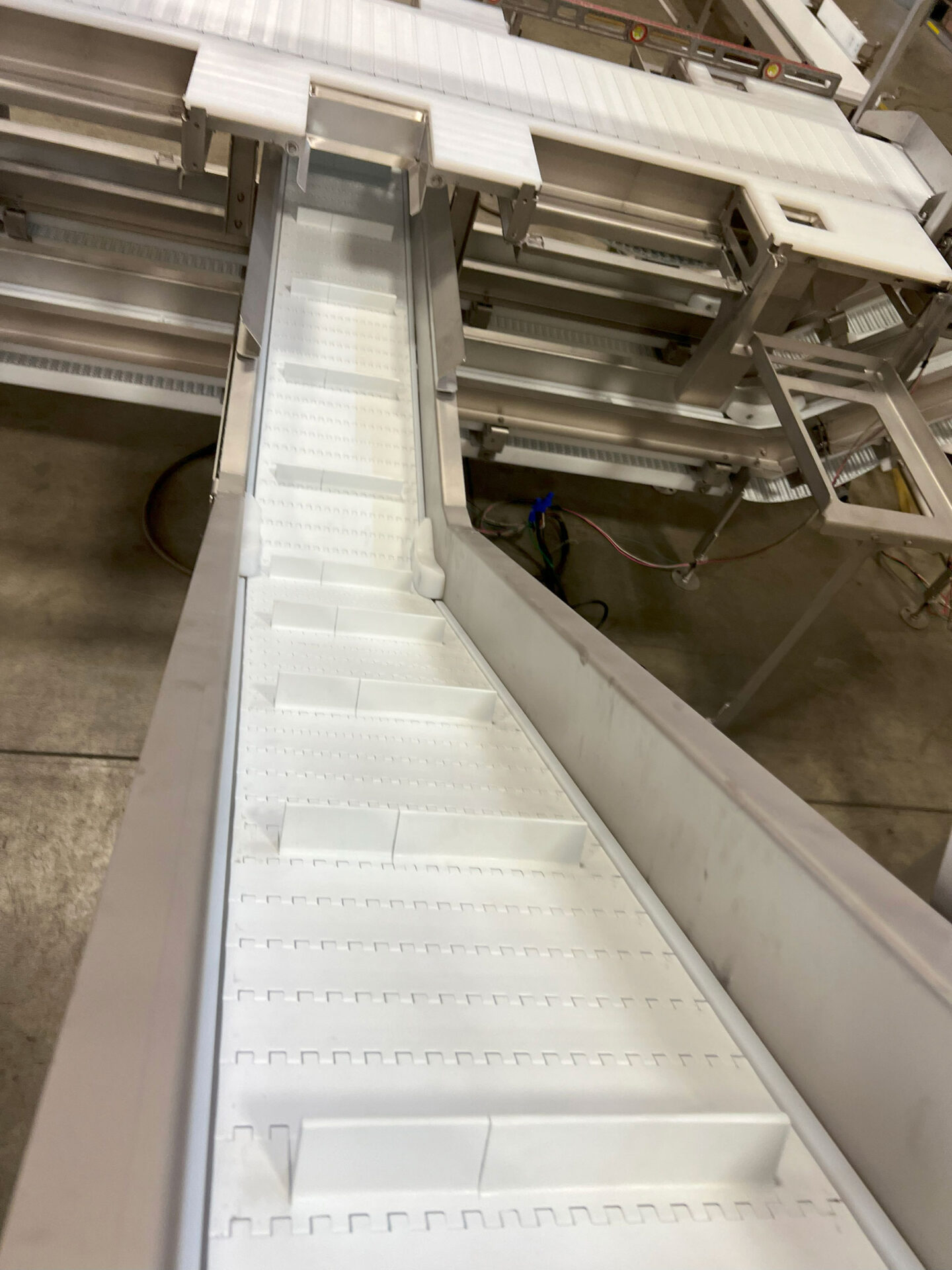 Box conveyor system designed for efficient material handling in food processing, featuring a white inclined conveyor belt with modular sections.