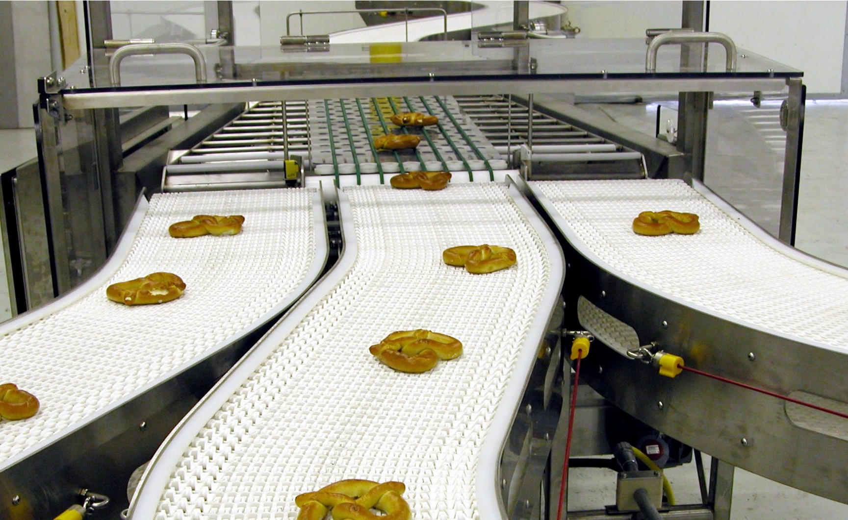 Conveyor system transporting baked goods, featuring curved white conveyor belts with pretzels, showcasing food processing automation by CHL Systems.