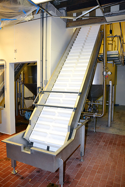 Custom conveyor system with inclined white plastic belt, designed for food processing and material handling, featuring stainless steel structure and integrated support in a processing facility.