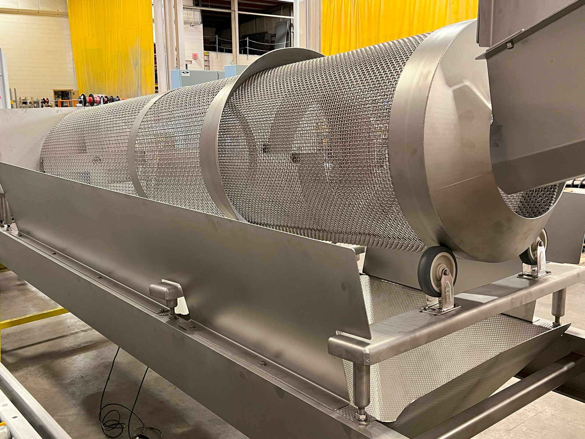 Custom material handling equipment featuring a cylindrical mesh drum within a stainless steel framework, designed for food processing automation.