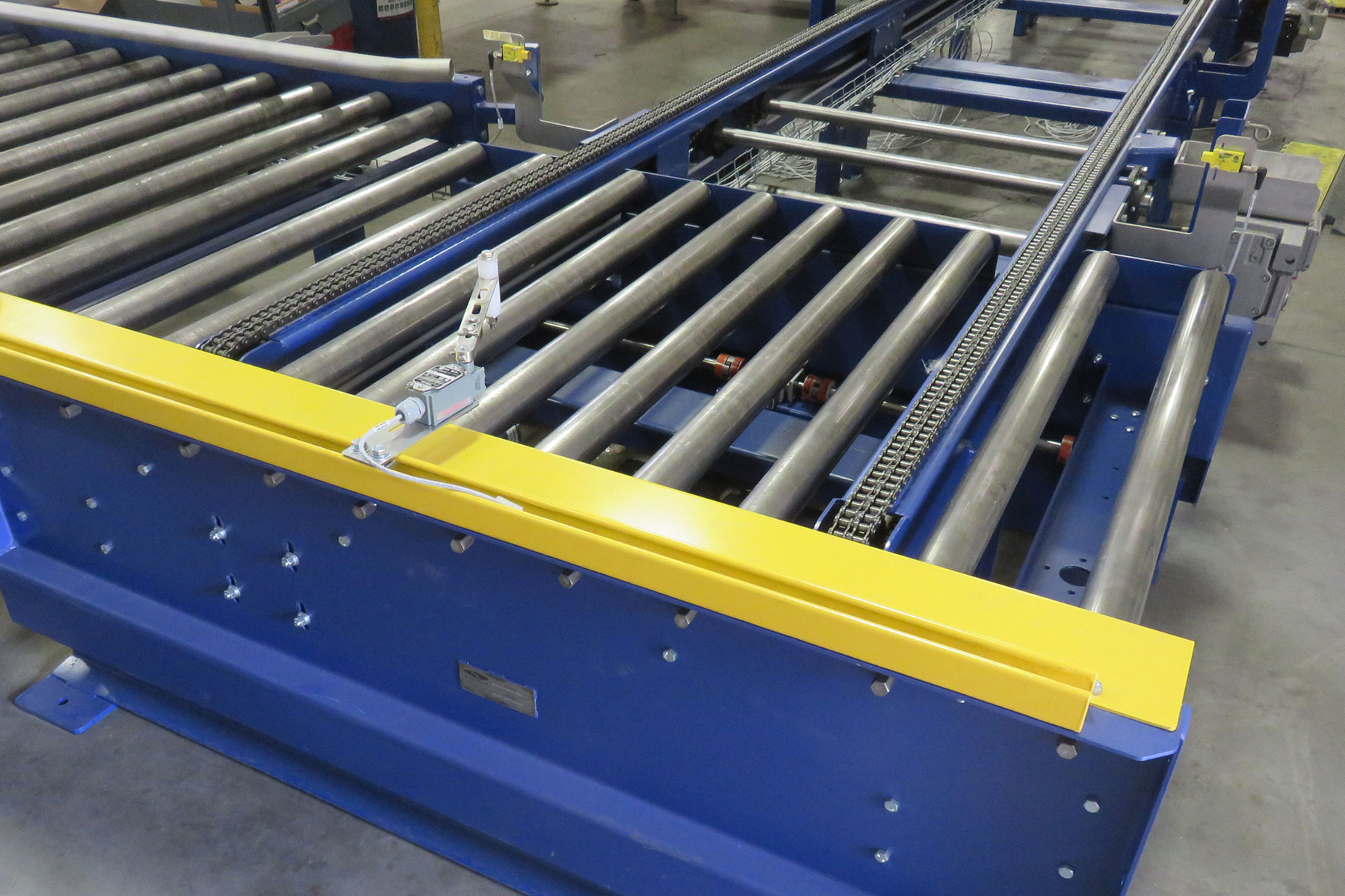 Drag chain conveyor system with metal rollers and yellow safety guard, designed for efficient material handling in food processing automation.