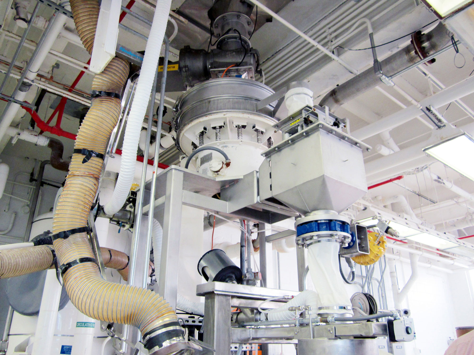 Drum filling and weighing station featuring industrial equipment, including a hopper, tubing, and conveyor system, designed for food processing automation by CHL Systems Inc.