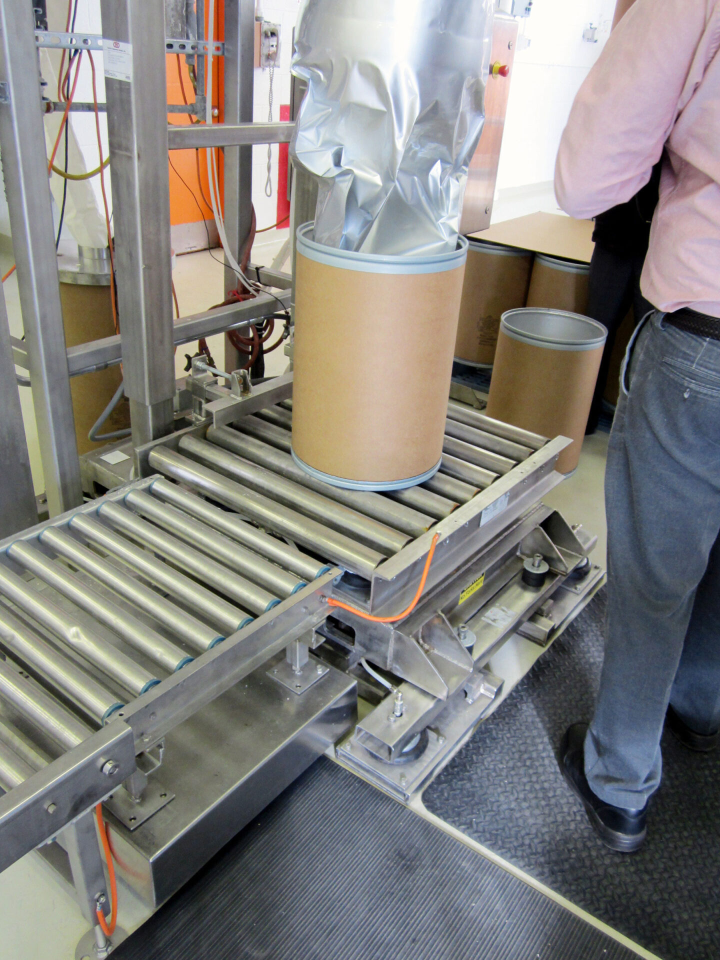 Drum filling and weighing station with conveyor system, featuring cylindrical containers and automated handling equipment, relevant to food processing and packaging solutions by CHL Systems.