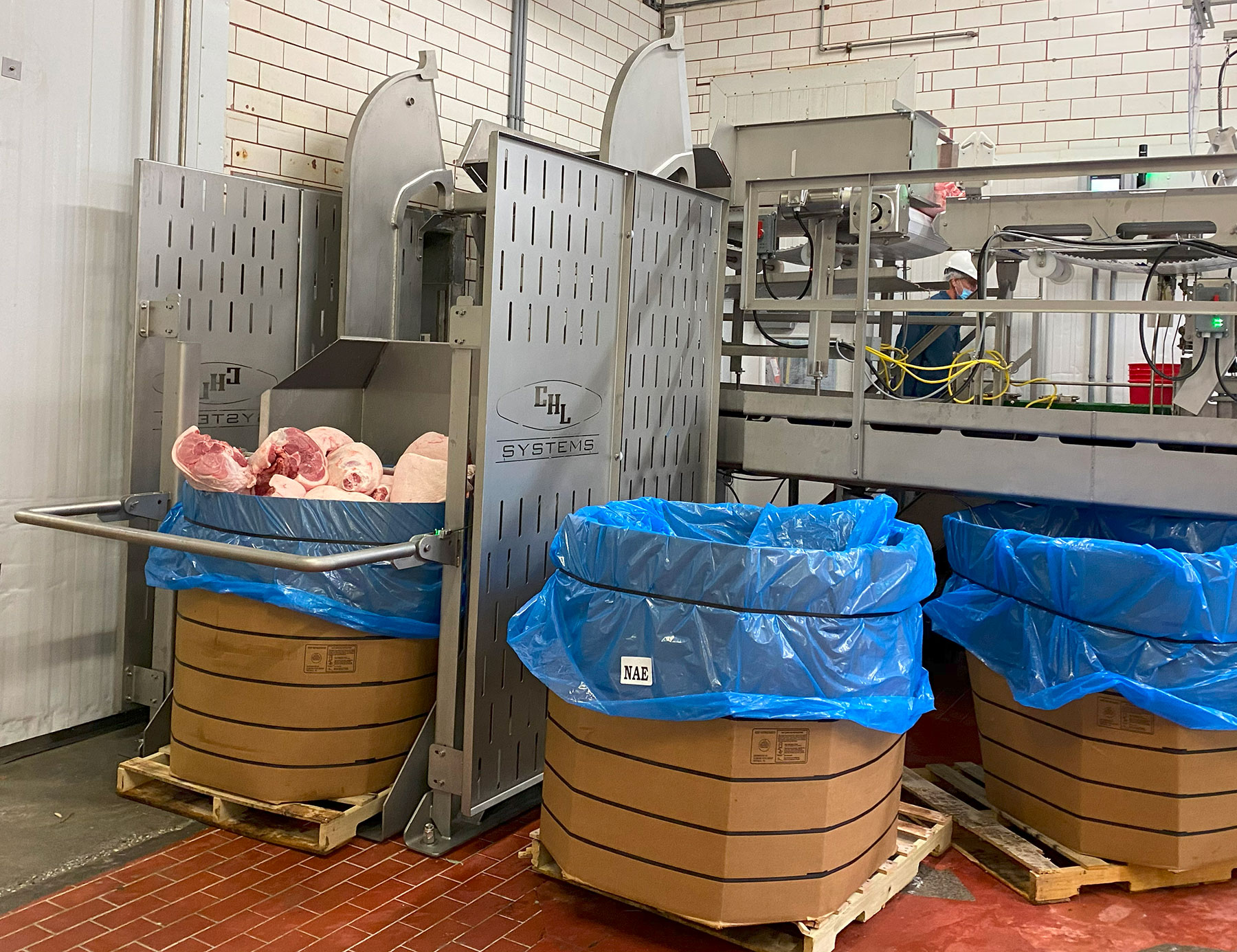 Dumper equipment by CHL Systems for food processing, featuring a stainless steel design, loaded with meat products, surrounded by large containers with blue liners.