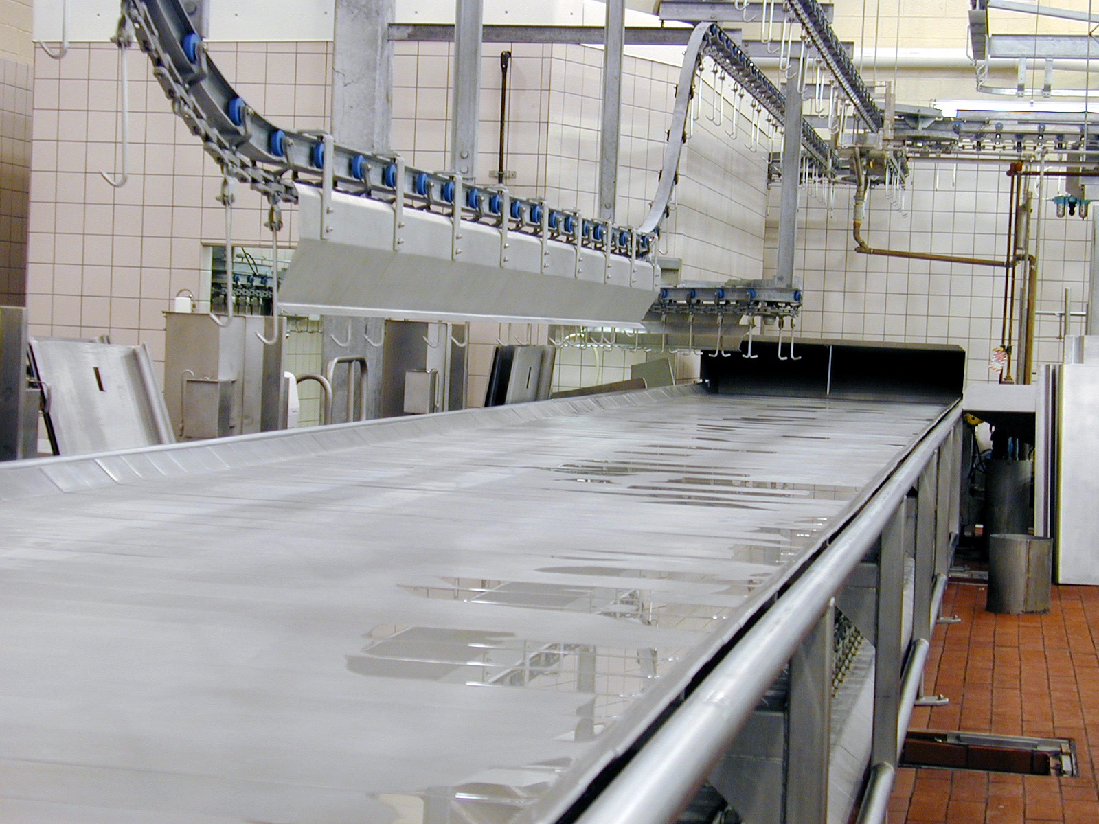 Harvesting line conveyor system in a food processing facility, featuring stainless steel surfaces and overhead mechanisms for efficient material handling.
