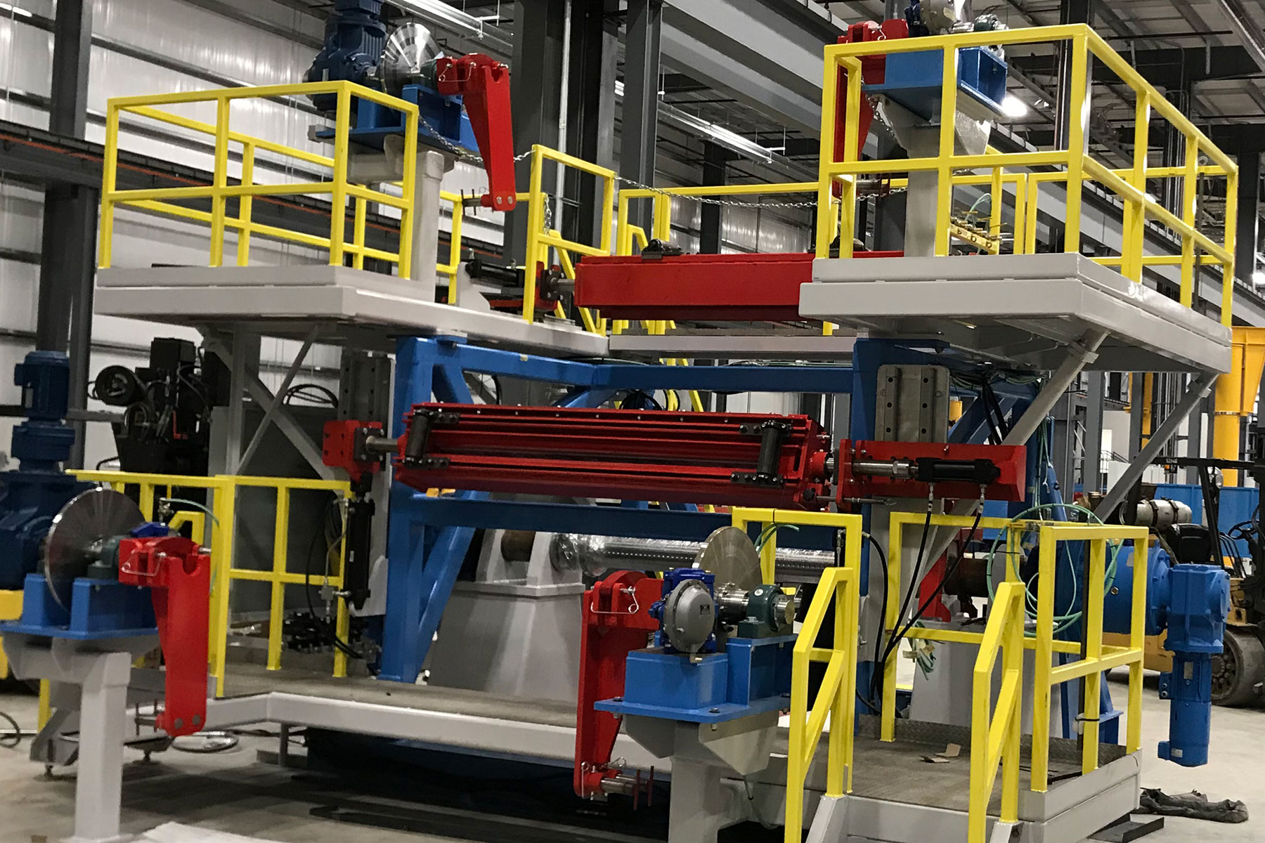 Metal coiler machinery with red and blue components, elevated platform with yellow safety railings, designed for food processing automation and material handling systems.
