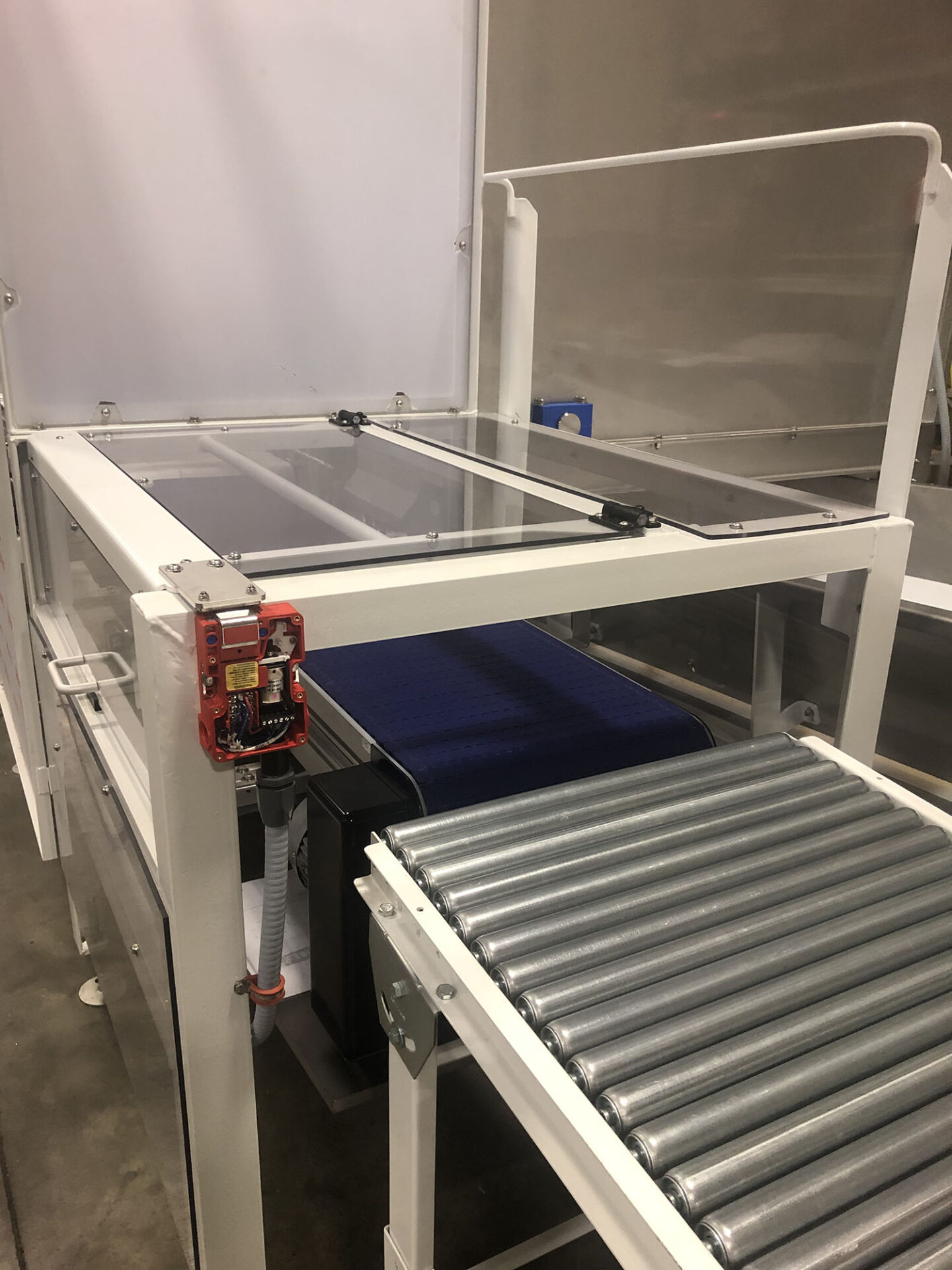 Metal detector conveyor system featuring a transparent safety cover, blue conveyor belt, and roller conveyor, designed for food processing automation by CHL Systems Inc.