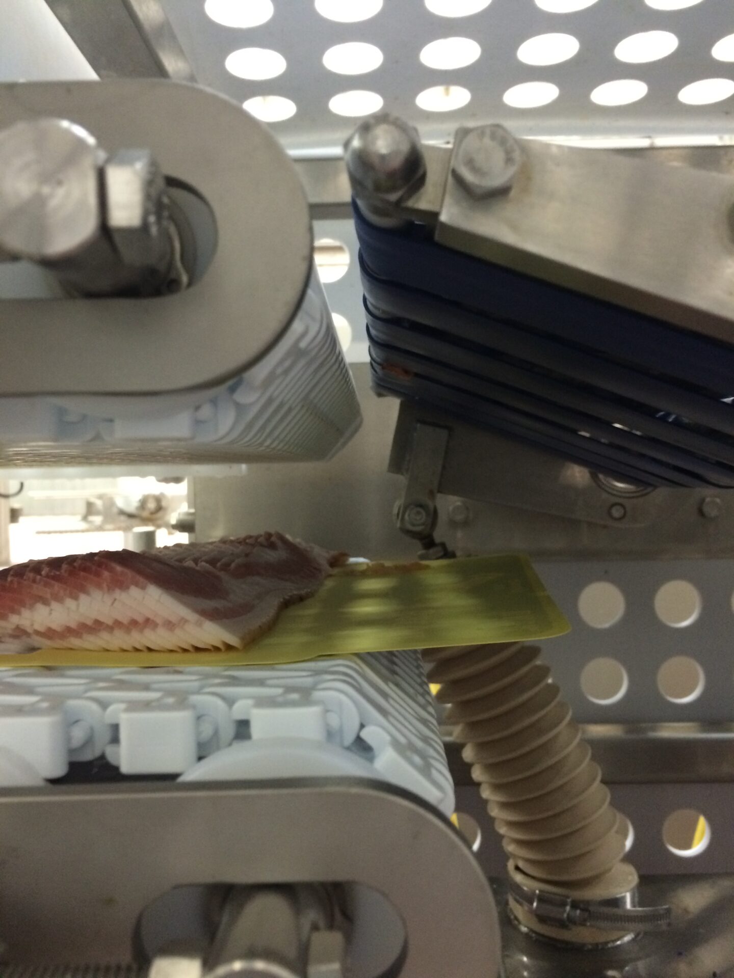 Conveyor system with sliced meat on a yellow tray, showcasing food processing automation equipment by CHL Systems.