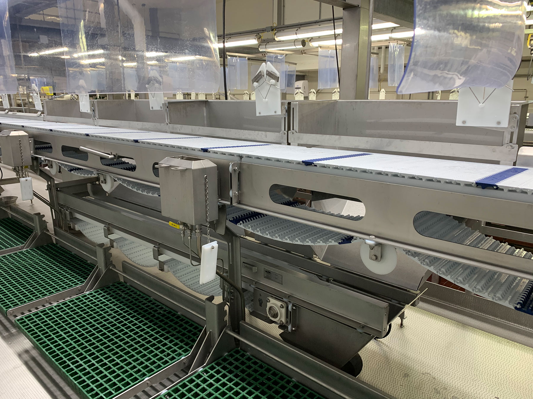Processing line conveyor system with stainless steel construction, featuring multiple conveyor belts, green drainage mats, and transparent protective barriers, designed for food production automation by CHL Systems.