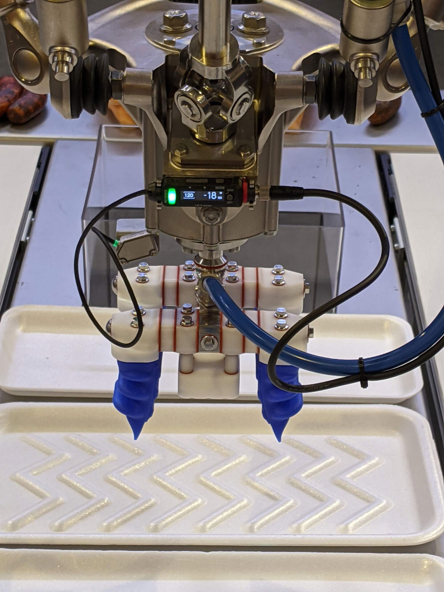 Robotic pick and place system with blue dispensing nozzles applying material onto a patterned tray, showcasing automation in food processing and packaging solutions by CHL Systems Inc.
