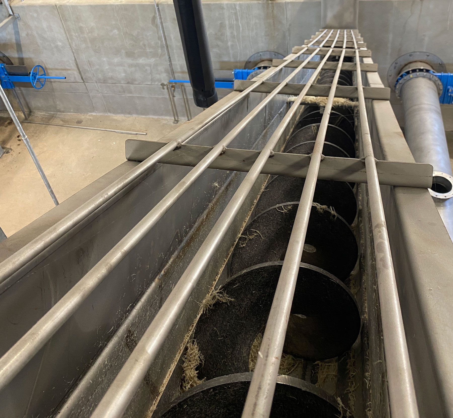 Screw conveyor system with metal augers and support rails in a food processing facility, showcasing CHL Systems' automation solutions for material handling.