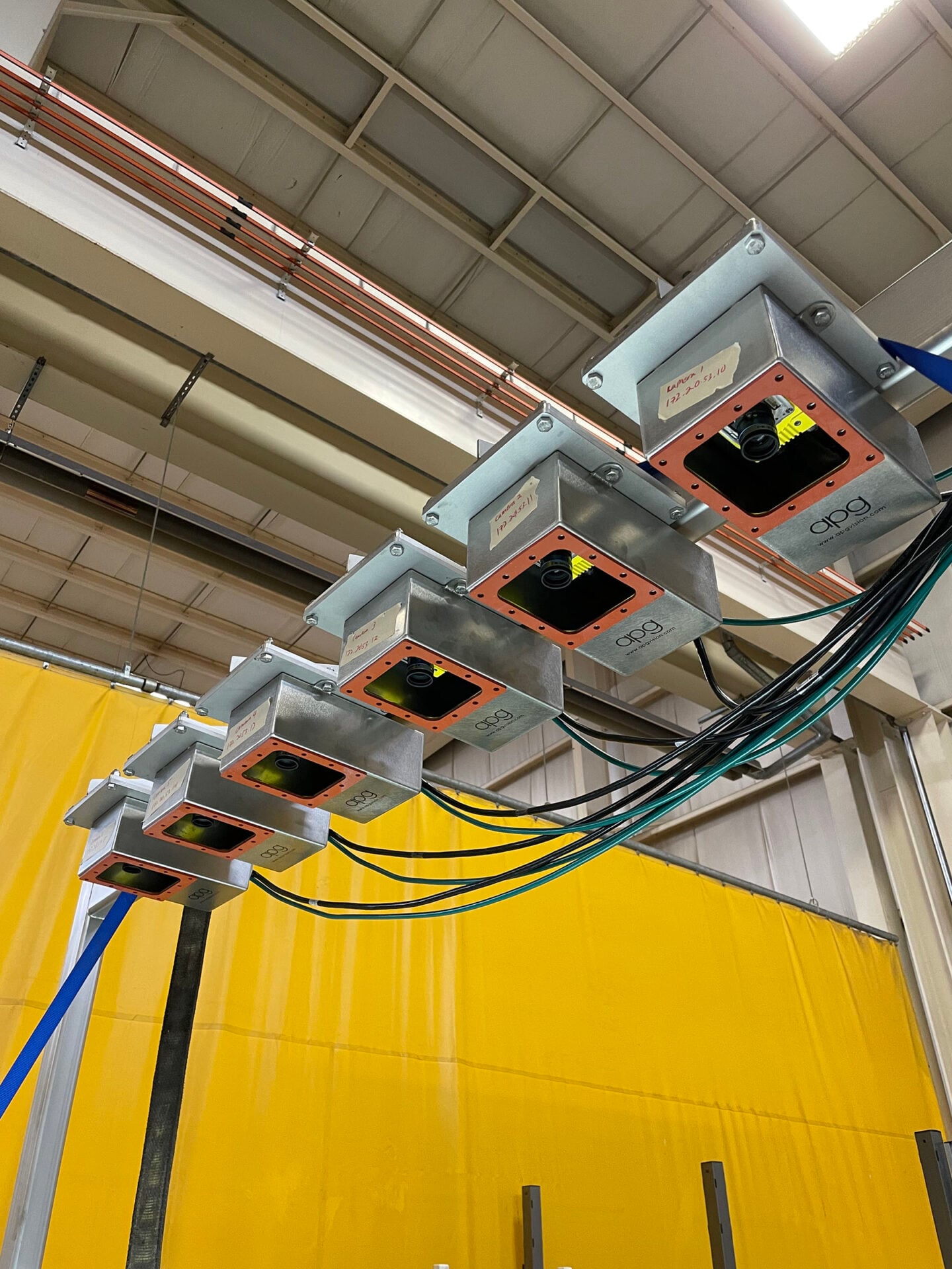 Vision inspection system with multiple cameras and wiring, set against a yellow backdrop in a food processing facility.