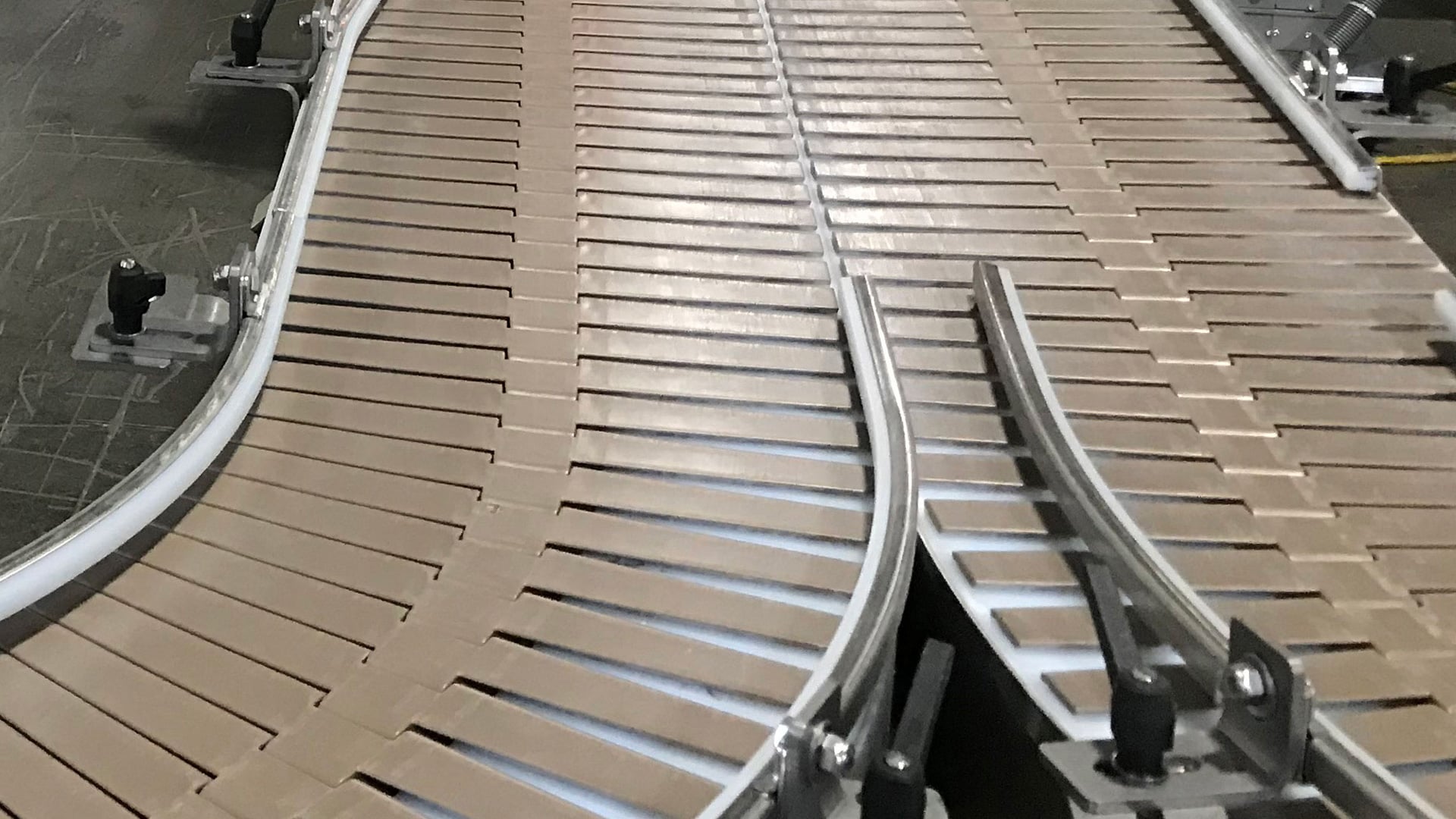 Slat conveyor system with interconnected slats on a curved path, designed for transporting irregularly shaped products in food processing applications.