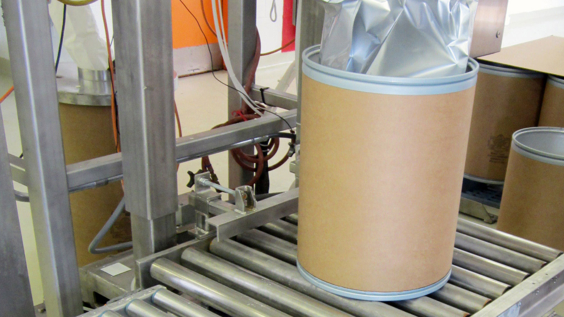 Weigh-station conveyor system with cylindrical containers on rollers, designed for accurate product weighing in food processing applications.